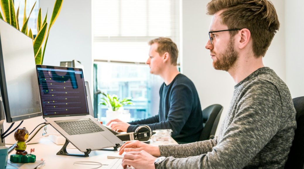 man sitting on chair wearing gray crew-neck long-sleeved shirt using Apple Magic Keyboard